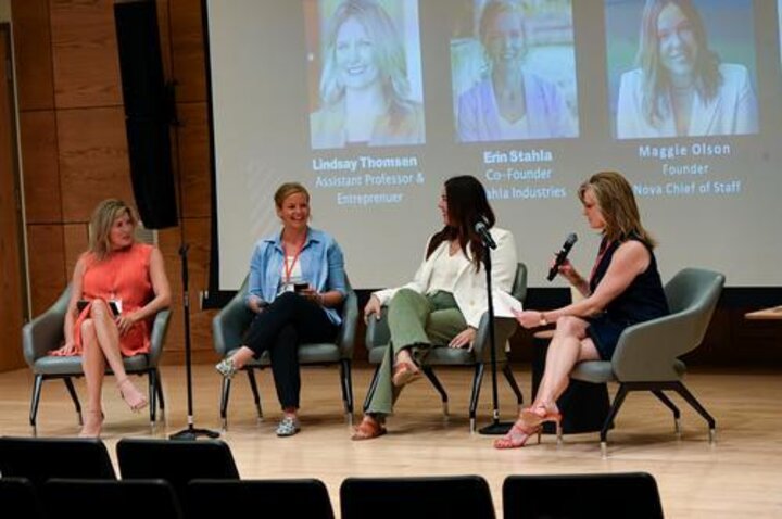 Four women seated in chairs on a stage, engaged in a panel discussion.
