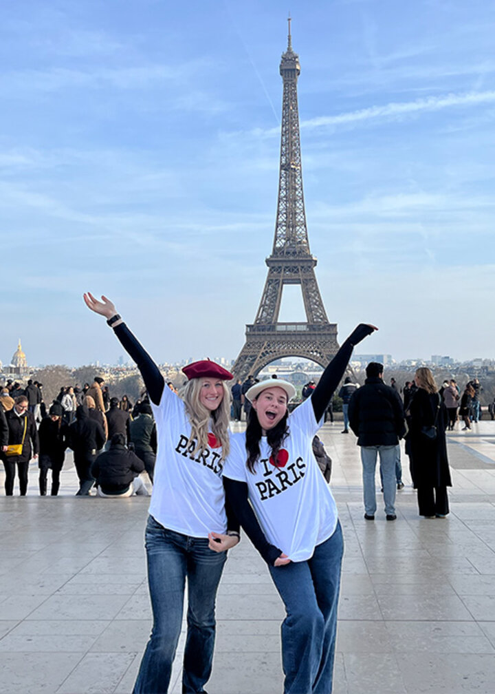 Collette and another female wear I heart Paris tshirts in front of the Eiffel Tower