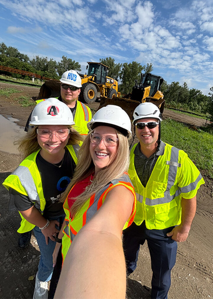 Collette and coworkers wear hard hats and reflective safety vests at a construction site
