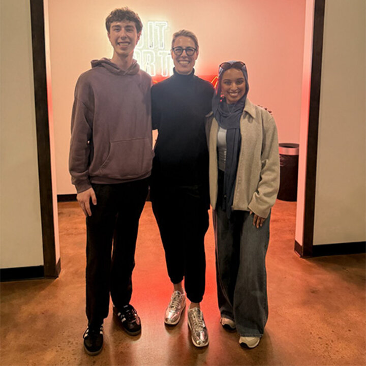 Two students flank Morgan Shaw Parker, who is wearing shiny sneakers, in her Atlanta office
