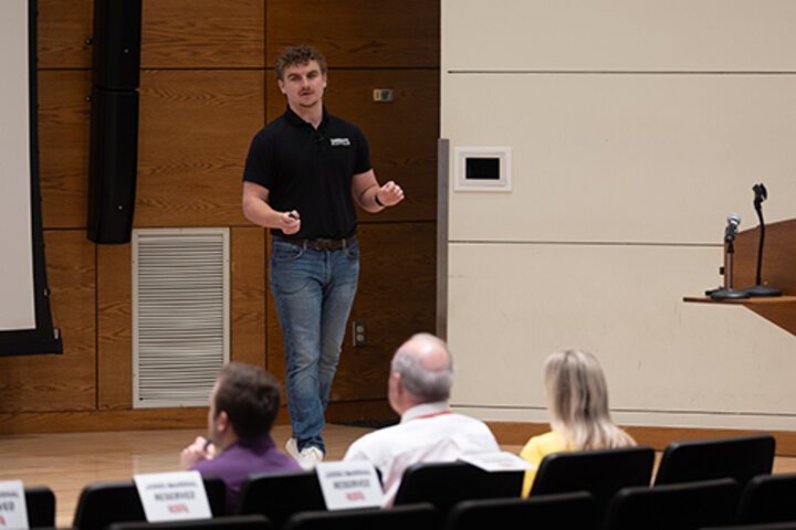 Speaker in a black shirt presents in front of an audience in a lecture room.