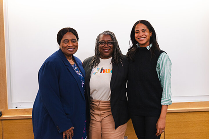 Three individuals standing together in a classroom setting, wearing professional attire.