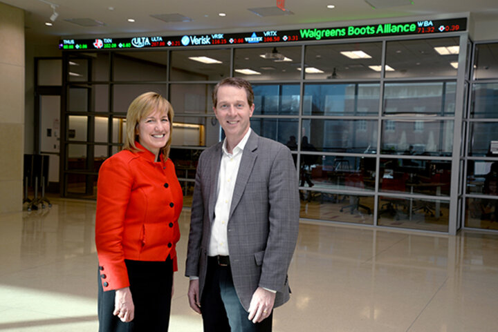 Dean Kathy Farrell and Paul West, '98, in front of the college’s state-of-the-art trading room.