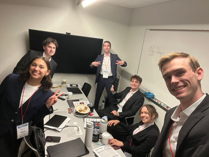 Group of people in business attire gathered around a conference table in a small office setting.