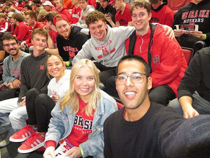 Smiling group of young adults in red and white outfits seated at a sports event.