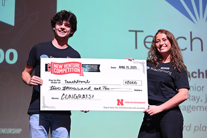 Two people on stage holding a large check for $2,000, celebrating a competition win.